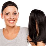 young woman with a wig cap on her head holding a wig in hand